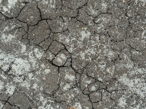Dry cracked dark earth dusted with light colored sand