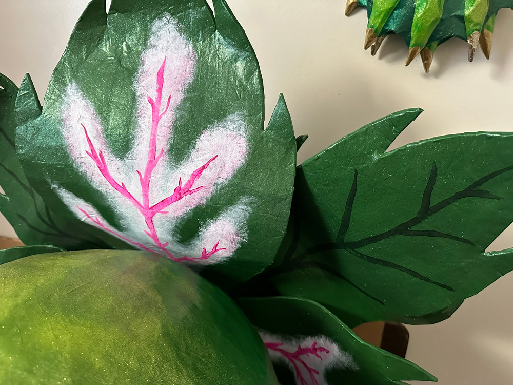 Close up of the big leaves behind Audrey's head; they're dark green with pink and white highlights in the middle.