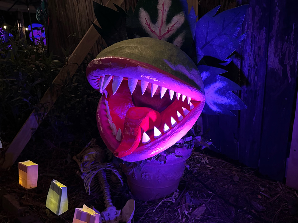 The Audrey II mask, sitting in a big flower pot, in spooky nighttime purple ourdoor lighting.