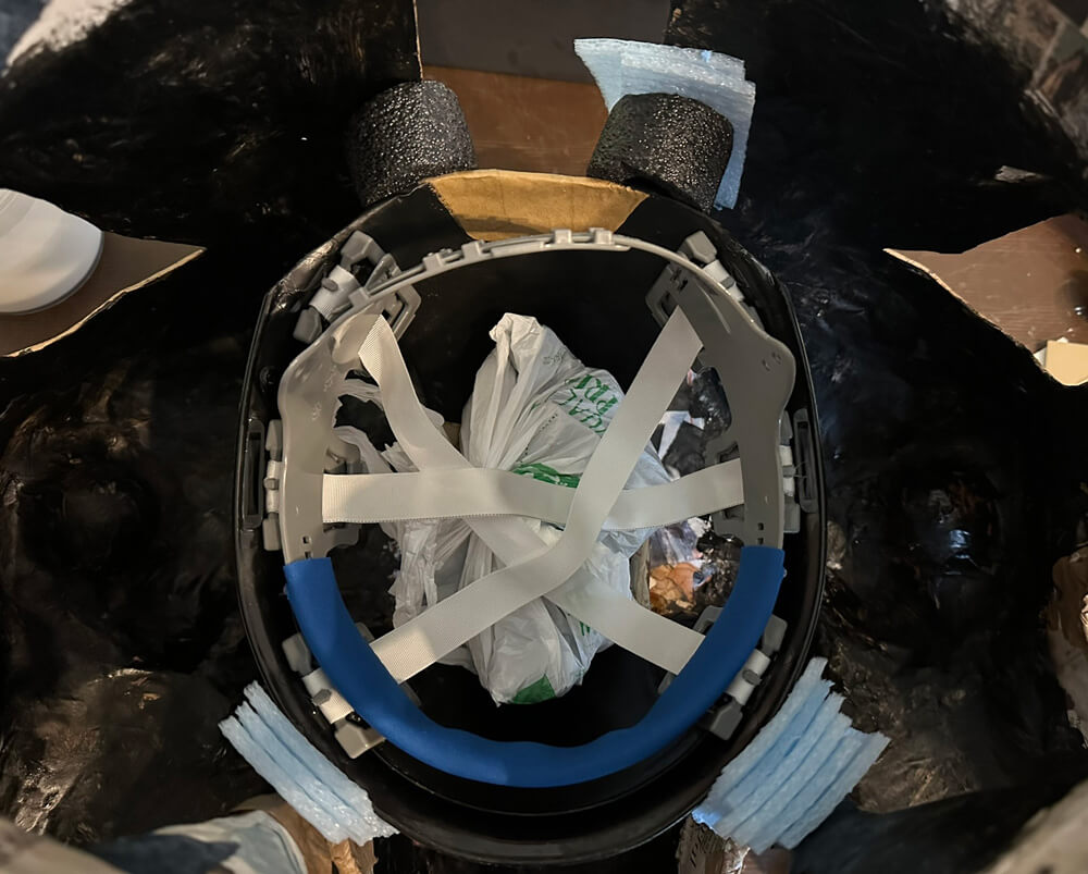 Downward view of the hard hat in the mask, with a shopping bag full of rocks sitting in it