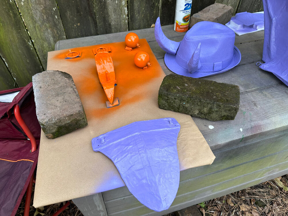 Various parts of the costume laid out on a board and spray painted orange and purple
