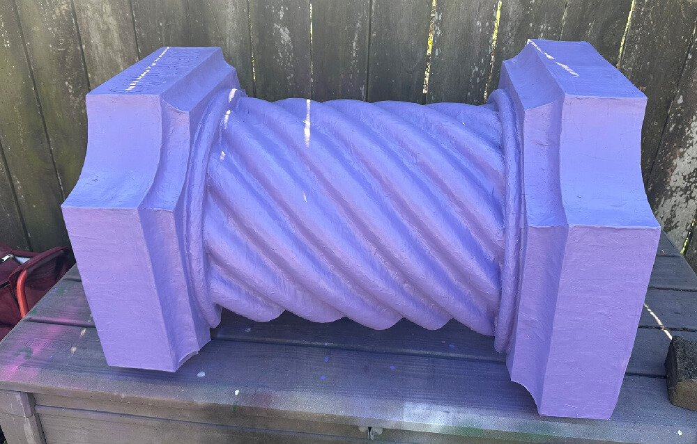 Fake stone column lying on its side, spray painted purple.