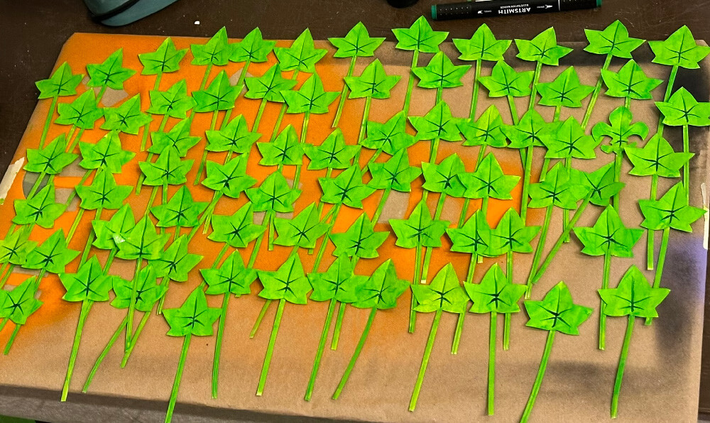Many fake ivy leaves laid out on a table, painted bright green.