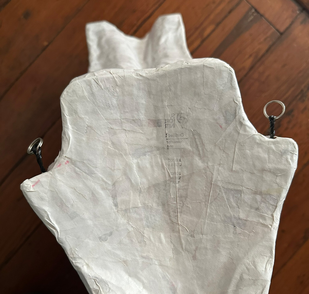 The structure on the back of the wings for hanging on the jacket; it's basically shaped like a guitar pick and has two metal key rings hanging by twist ties at the top corners