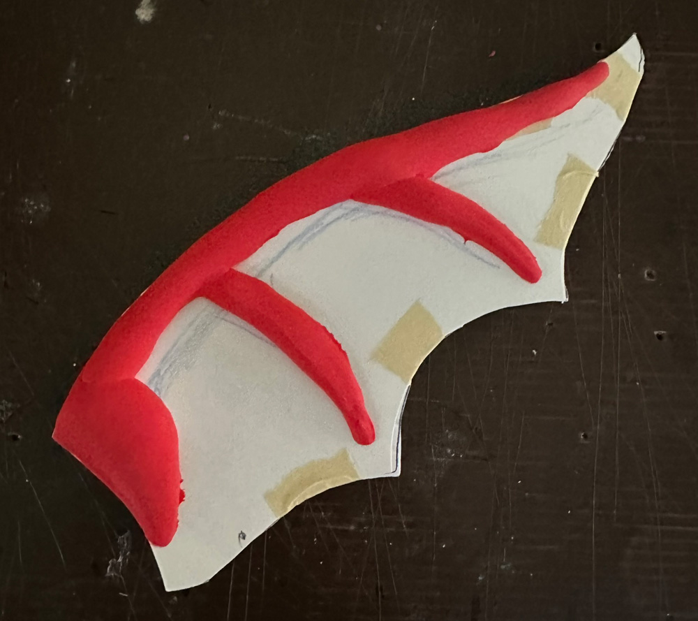 An ear, shaped roughly like a bat wing, with ridges built up from red foam clay