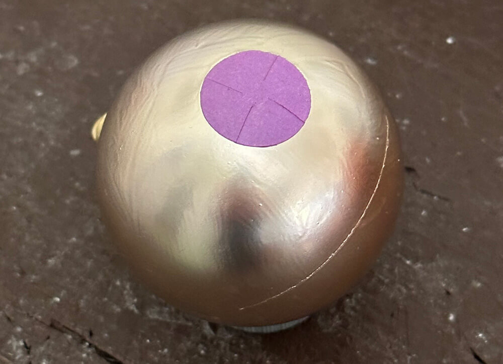Christmas ornament with a purple circle glued onto it; some cuts are visible on the circle