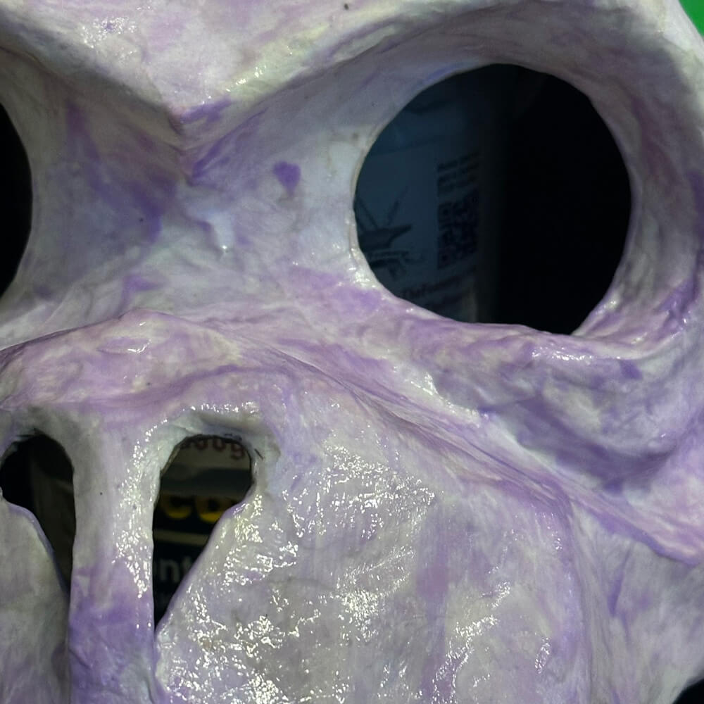 Close up of the gargoyle's eye and nose; the whole surface is covered with blotchy light purple paint