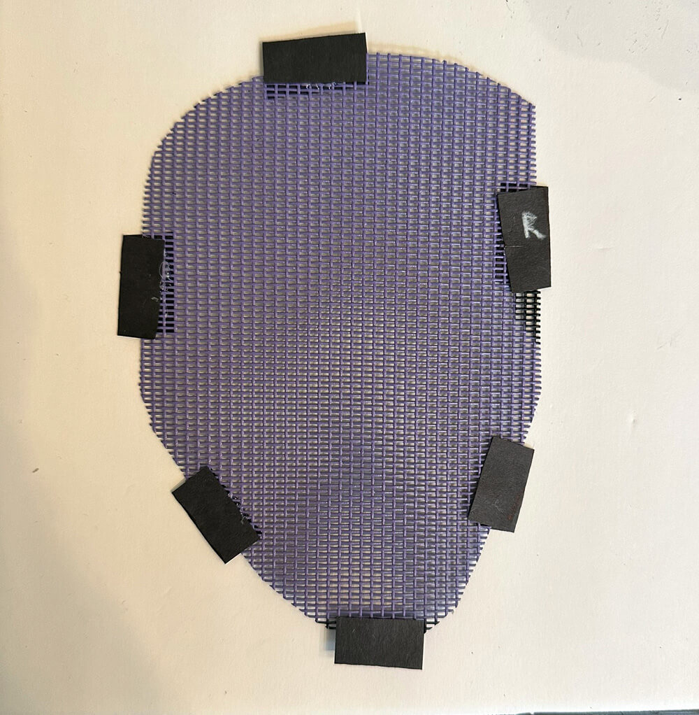Close up of a piece of purple screen with six small black paper tabs glued around the edges.