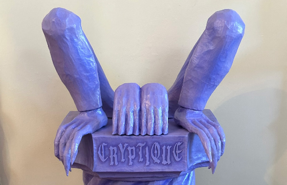 A pair of crouched legs made of paper mache, with monster feet with long pointy toes. A pair of hands is perched between them. Everything in painted purple.