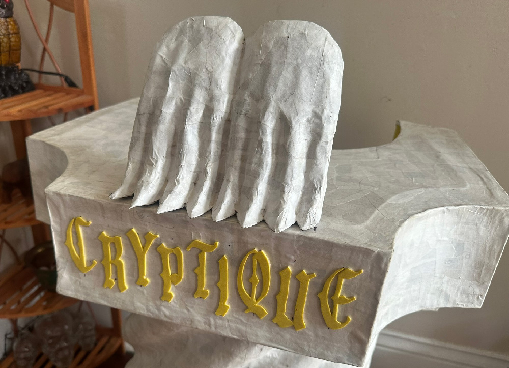 The paper mache hands, not yet painted, perched on the top of the fake stone column, with the word Cryptique on it.