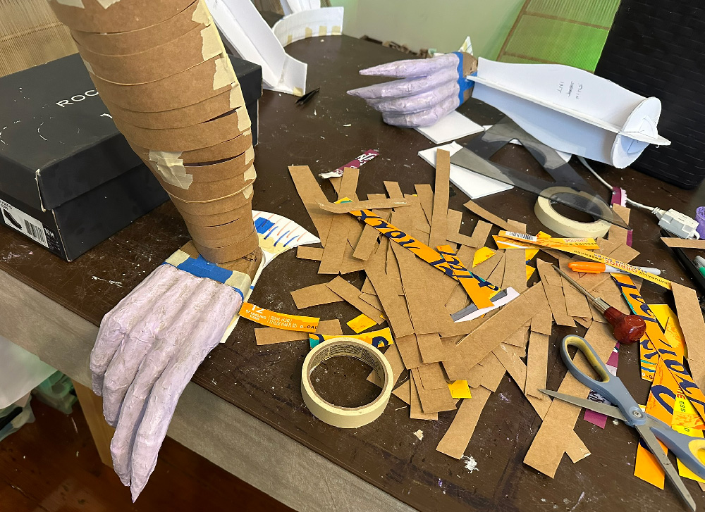 Thin strips of brown pasteboard wrapped around the armature of a leg, giving it a more realistic rounded shape.