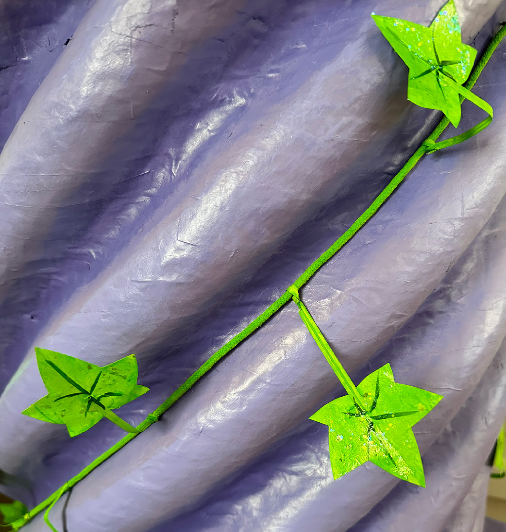 A green vine with green leaves wrapping around the spiral ridges of the paper mache column