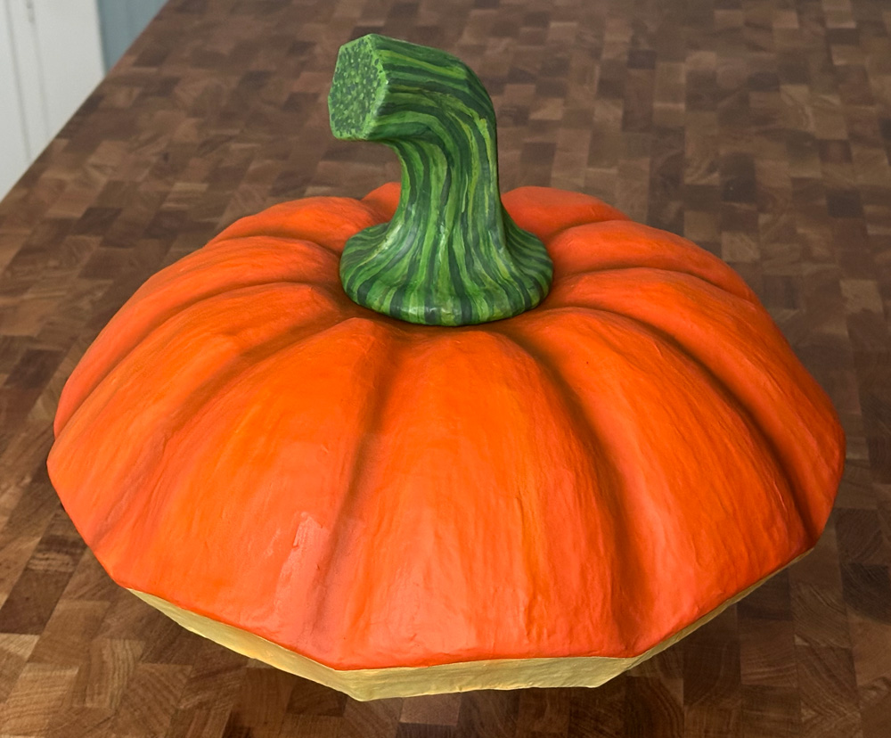 My paper mache pumpkin lid hat sculpture, painted orange and with a green stem.