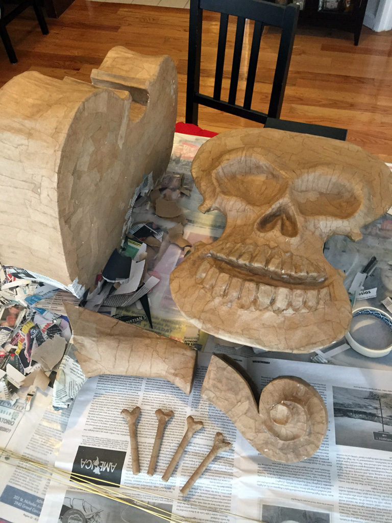 Separate pieces of my violin skull mask laying on a table, covered in brown paper mache, not yet assembled and painted.