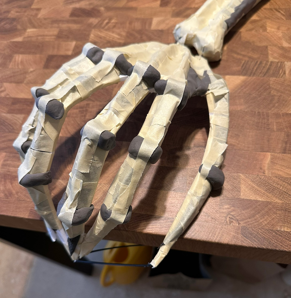 Close up of the hand showing little blobs of gray foam clay as bony knuckles.