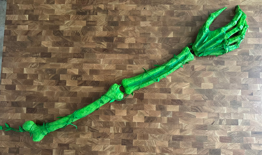 The whole arm laying on a table, showing the subtle darker green shading and with the fake vines and leaves wrapped around.