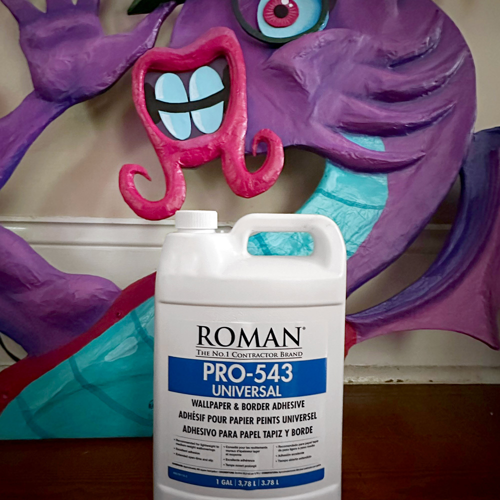 A bottle of Roman Pro-543 Universal wallpaper adhesive sitting in front of my paper mache Jabberwocky sculpture