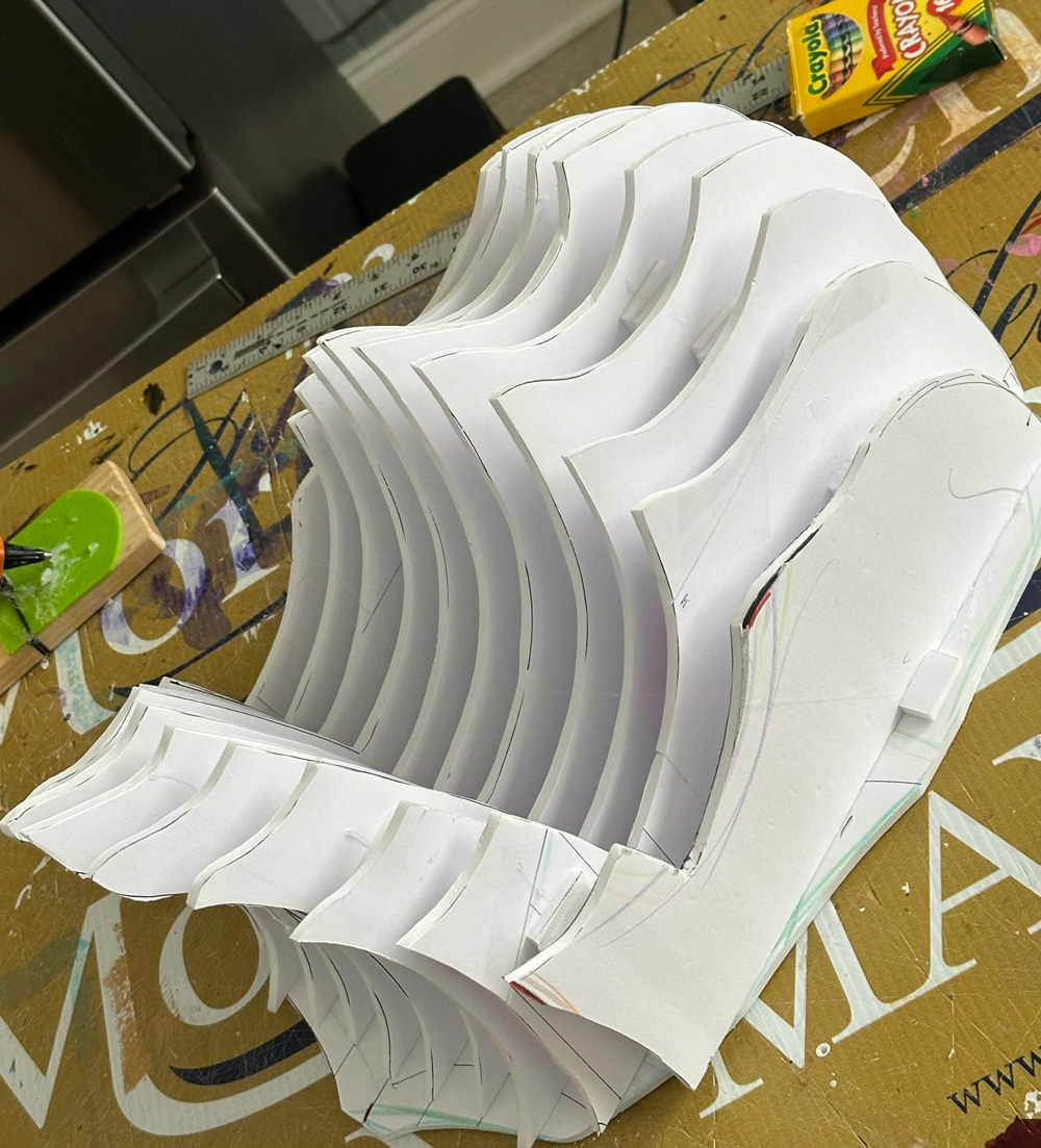 A simple foam board armature of a face with a large open mouth, laying flat on a table.