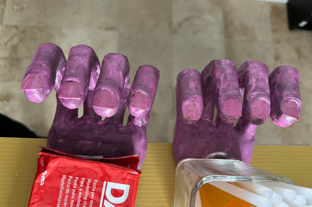 Early stages of painting; the hands are purple and pink and the texture looks rough.