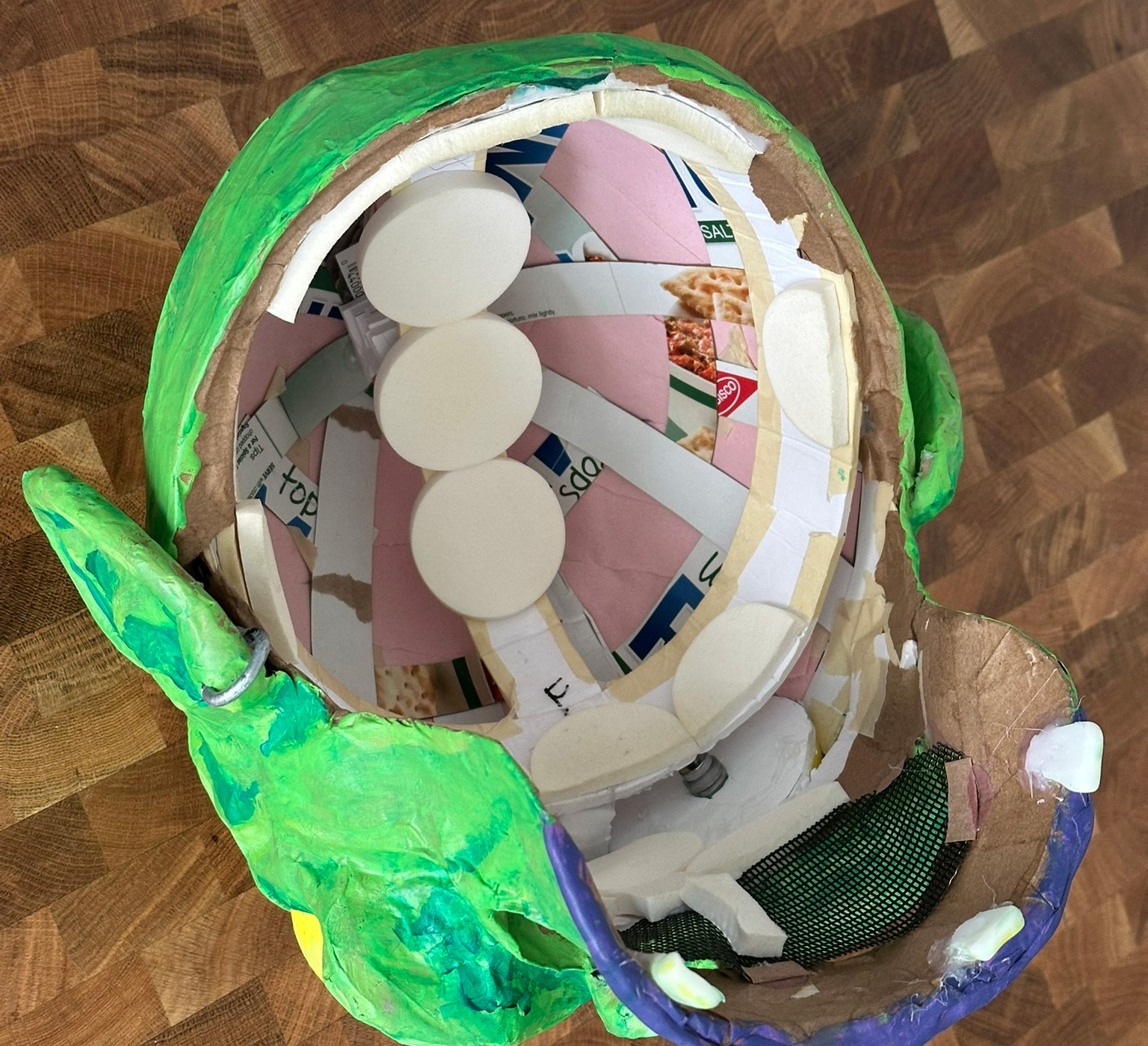 The interior of the mask, showing the pasteboard strips and pink construction paper lining the top, and the makeup pads lining the wearable headband part.