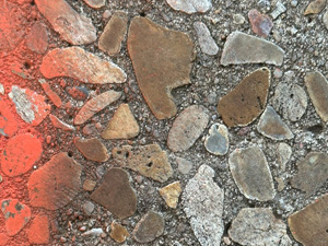 A section of sidewalk that has been ground down so the rocks inside are all flat and smooth. There's some orange spray paint along one side.