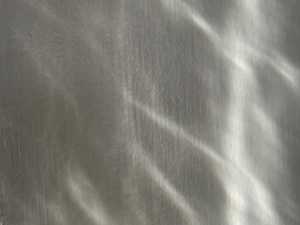 A wispy white pattern on a gray wall from sunlight coming through an old window pane.