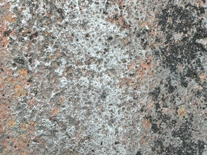 A very corroded gray metal surface with some brown rusty bits and black stains.
